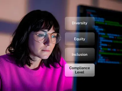A woman in a pink shirt and glasses focuses on a computer screen displaying code, with text on diversity, equity, inclusion, and compliance.