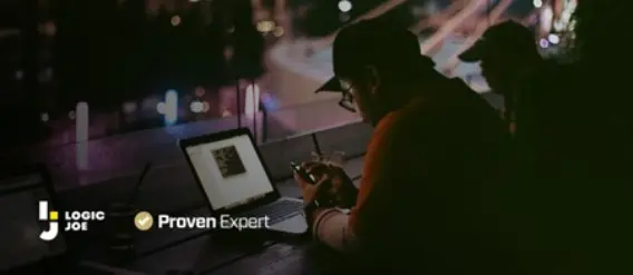 A person sitting at a dimly lit table, using a smartphone, with a laptop and city lights in the background.