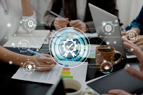 A group meeting with hands on documents and a laptop, featuring digital icons representing quality assurance and collaboration.