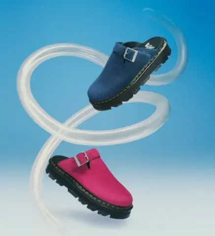 Two clogs, one blue and one pink, are suspended in mid-air, intertwined with a clear, swirling tube against a blue background.