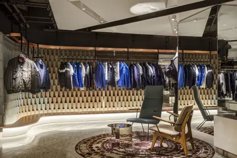 A modern clothing store interior featuring a display of jackets on hangers, two stylish chairs, and a decorative rug.
