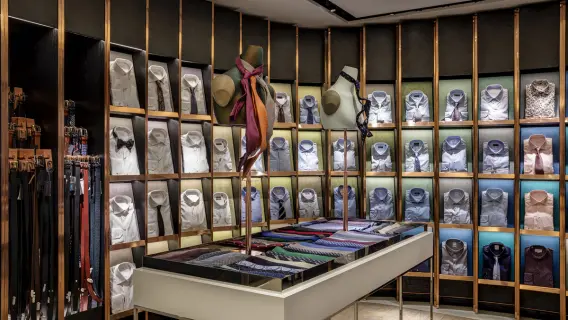 A stylish clothing store display featuring neatly arranged dress shirts, ties, and belts on shelves and a central table.