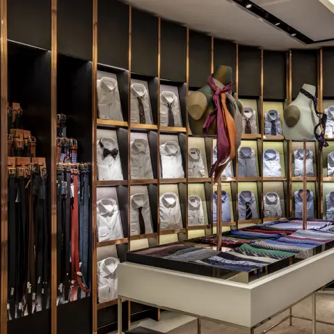 A stylish clothing store display featuring neatly arranged dress shirts, ties, and belts on shelves and a central table.