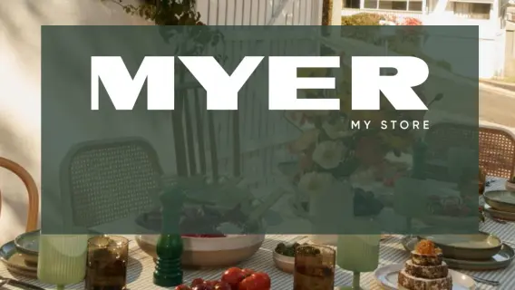 A beautifully set outdoor dining table with various dishes, drinks, and flowers, featuring the Myer logo prominently displayed.