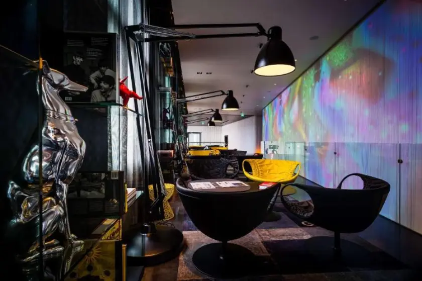 A modern lounge featuring sleek black and yellow furniture, artistic lighting, and colorful projections on the wall.