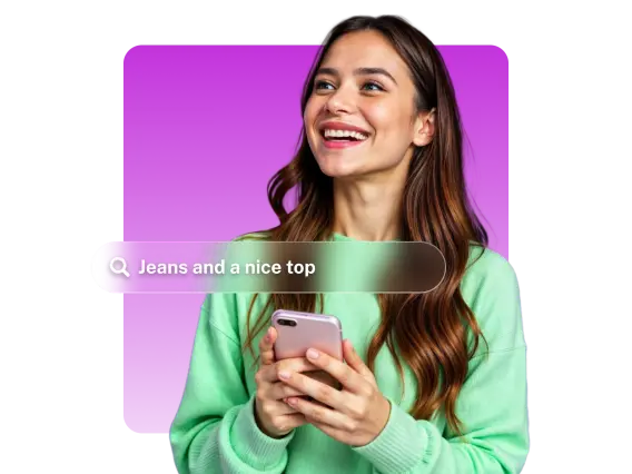 A smiling woman in a green sweater holds a smartphone, with a search bar displaying 'Jeans and a nice top' in front of her.